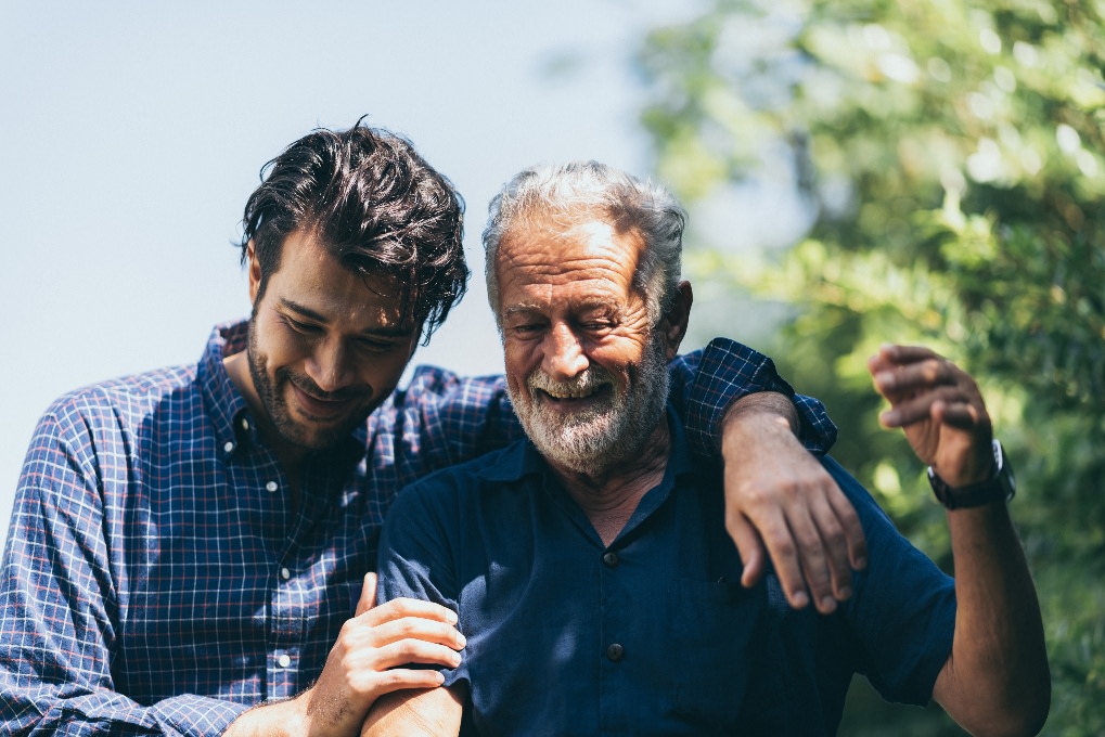 Father with his adult son's arms around him smiling in the sunshine